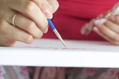 Sanat. Sayılarla çizim. Bir kadın bir tuval pamuk boyar. Fırçalar, boyalar ve su bir bardak sayılı kullanır.