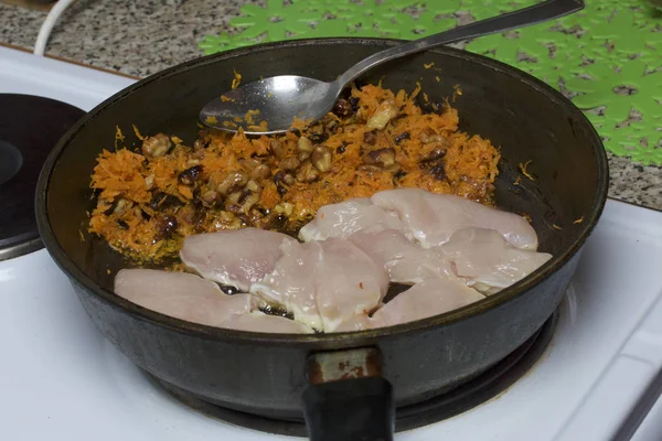 Beredning av kycklingfilé i en stekpanna. Köttet är stekt tillsammans med morötter och valnötter. — Stockfoto
