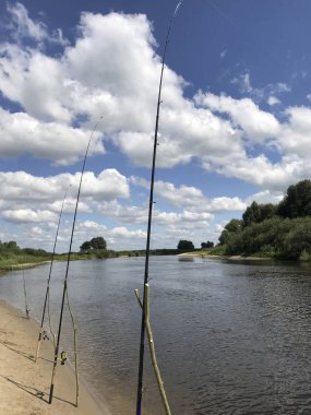 Nehir kıyısında boyunca balıkçılık çubuklar. Harika nehir manzara. Bulutlar gökyüzünde bir sürü.