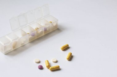 Tabletler ve hapları bir kaba tabletler için haftanın günlerini yayılmıştır. İlaçlar farklı şekiller ve renkler. Birkaç tablet masa etrafında dağılmış.