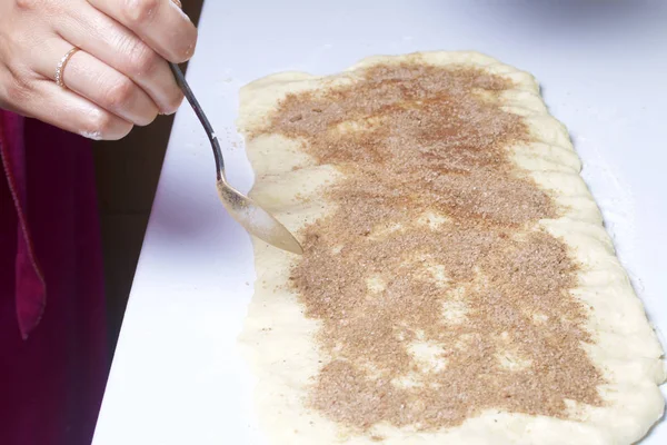Женщина готовит булочки с корицей. Она закатывает начинку на катанное тесто. Смешанный сахар и корица . — стоковое фото