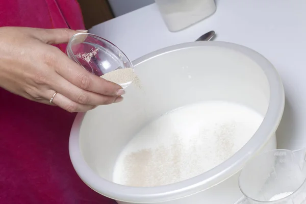 Ingredientes para fazer rolos de pastelaria. A mulher adiciona o fermento ao leite aquecido . — Fotografia de Stock