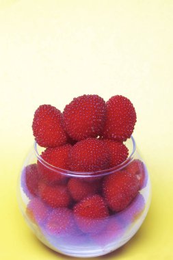 Büyük kırmızı meyveler bir cam vazo içinde ahududu benzer. Sarı bir arka plan üzerinde. Yukarıdan görüntülemek.