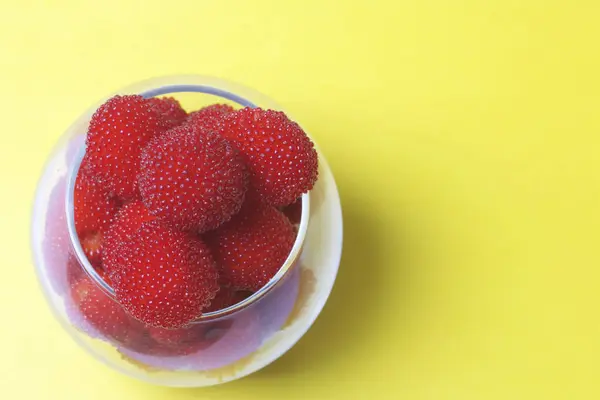 Large red berries are similar to raspberries in a glass vase. On a yellow background. View from above. — Stock Photo, Image