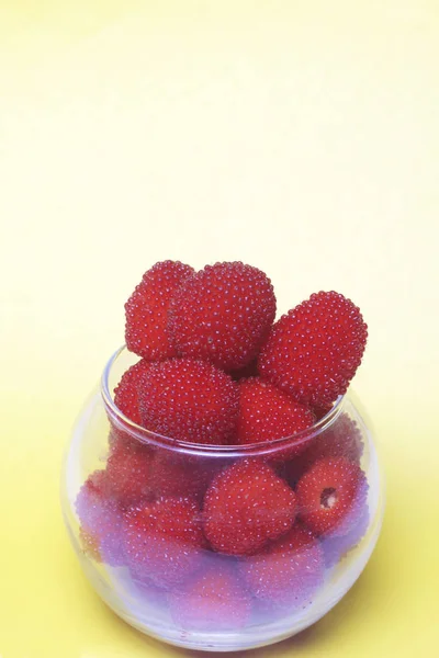 Las bayas rojas grandes son similares a las frambuesas en un jarrón de vidrio. Sobre un fondo amarillo. Vista desde arriba . —  Fotos de Stock