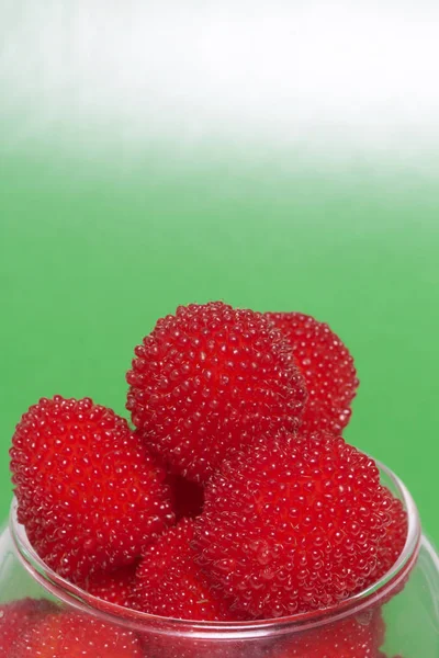 As grandes bagas vermelhas são semelhantes a framboesas em um vaso de vidro. Num fundo verde. Vista de cima . — Fotografia de Stock