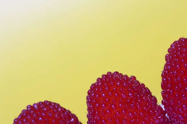 Velké červené bobule jsou podobné maliny. Na žlutém podkladu. — Stock fotografie