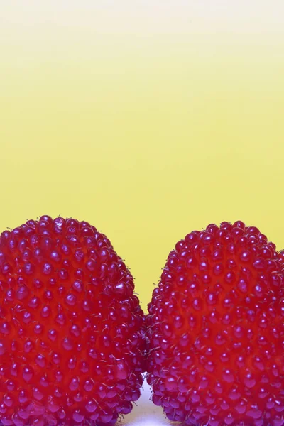 Velké červené bobule jsou podobné maliny. Na žlutém podkladu. — Stock fotografie