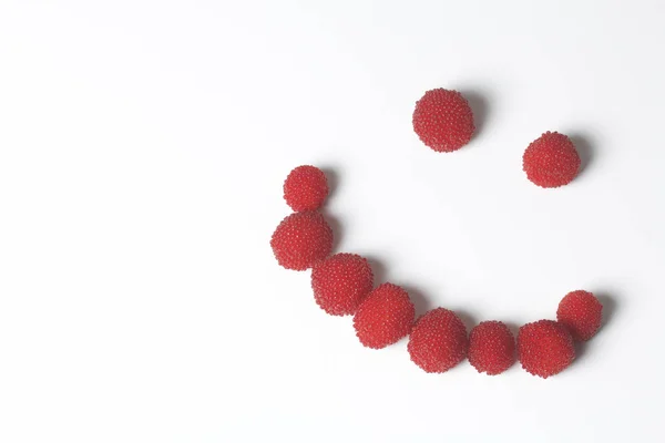 Large red berries are similar to raspberries. In the form of a smiling smiley. On a white background. — Stock Photo, Image