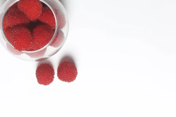 Las bayas rojas grandes son similares a las frambuesas en un jarrón de vidrio. Sobre un fondo blanco. Vista desde arriba . —  Fotos de Stock