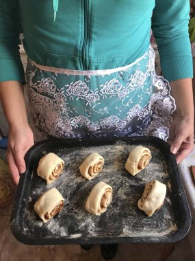 Evde tarçın ile buns hazırlanması. Bir kadın apronda fırın tepsisi topuz rulo ile taşıyabilir.