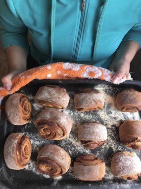 Evde tarçın ile buns hazırlanması. Kadın bir fırın tepsisi topuz ile rulo tutuyor.