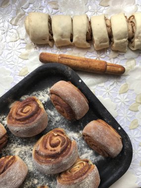 Evde tarçın ile buns hazırlanması. Hazır buns fırın tepsisine yalan. Tablo yanında bazı ham demir çubuklar ve ahşap bir oklava vardır.
