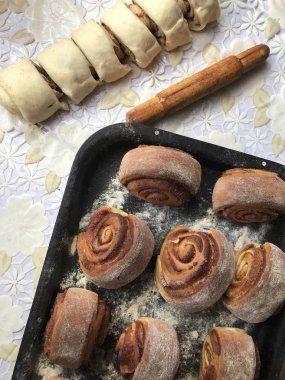 Evde tarçın ile buns hazırlanması. Hazır buns fırın tepsisine yalan. Tablo yanında bazı ham demir çubuklar ve ahşap bir oklava vardır.