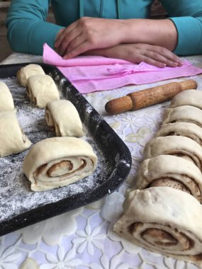 Evde tarçın ile buns hazırlanması. Ham buns fırın tepsisine yalan. Tablo yanında bazı ham demir çubuklar ve ahşap bir oklava vardır. Aşçı masada, ellerini sıktı oturur..