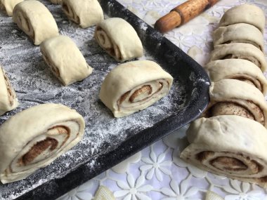 Evde tarçın ile buns hazırlanması. Ham buns fırın tepsisine yalan. Tablo yanında bazı ham demir çubuklar ve ahşap bir oklava vardır.