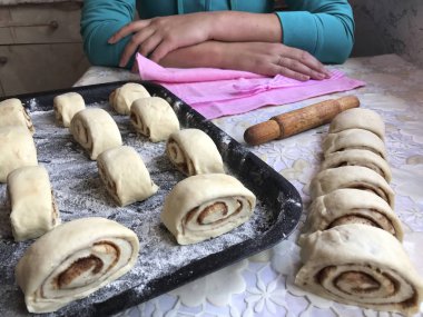 Evde tarçın ile buns hazırlanması. Ham buns fırın tepsisine yalan. Tablo yanında bazı ham demir çubuklar ve ahşap bir oklava vardır. Aşçı masada, ellerini sıktı oturur..