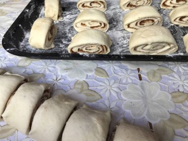 Evde tarçın ile buns hazırlanması. Ham buns fırın tepsisine yalan. Tablo yanında bazı ham demir çubuklar ve ahşap bir oklava vardır.