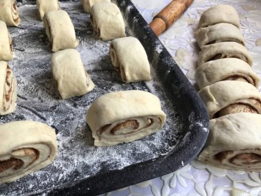 Evde tarçın ile buns hazırlanması. Ham buns fırın tepsisine yalan. Tablo yanında bazı ham demir çubuklar ve ahşap bir oklava vardır.