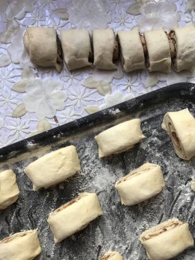 Evde tarçın ile buns hazırlanması. Ham buns fırın tepsisine yalan. Tablo yanında bazı ham demir çubuklar ve ahşap bir oklava vardır.