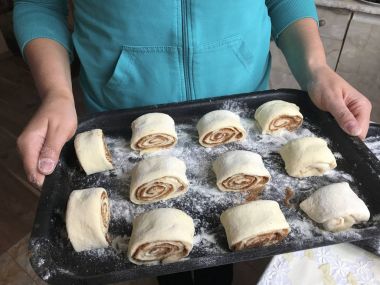 Evde tarçın ile buns hazırlanması. Kadın bir fırın tepsisi topuz ile rulo tutuyor.