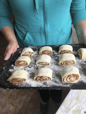 Evde tarçın ile buns hazırlanması. Kadın bir fırın tepsisi topuz ile rulo tutuyor.