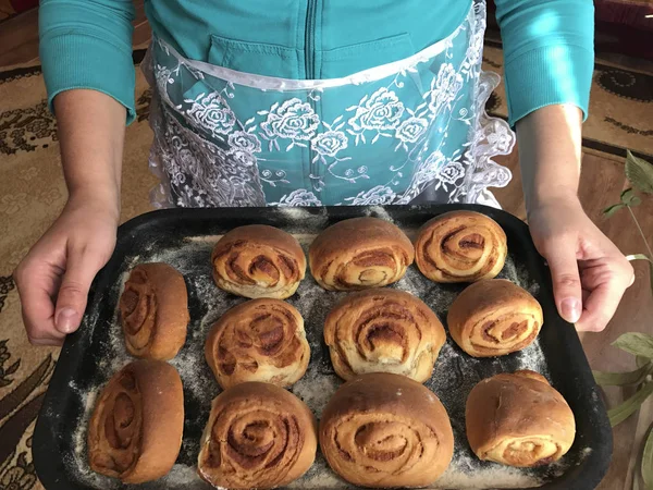 Preparation of buns with cinnamon at home. A woman in an apron holds a baking tray with bun rolls. — Stock Photo, Image