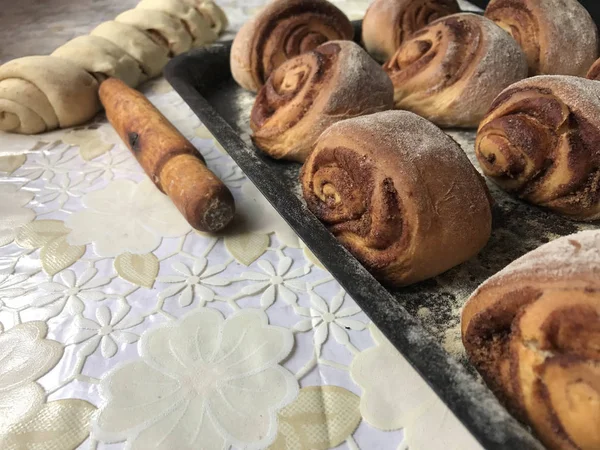 Evde tarçın ile buns hazırlanması. Hazır buns fırın tepsisine yalan. Tablo yanında bazı ham demir çubuklar ve ahşap bir oklava vardır.