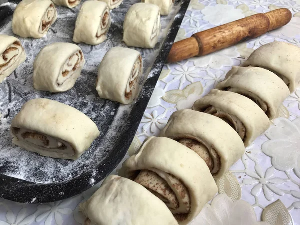 Zubereitung von Semmeln mit Zimt zu Hause. Rohe Brötchen liegen auf einem Backblech. Neben dem Tisch liegen ein paar rohe Knüppel und ein Nudelholz. — Stockfoto