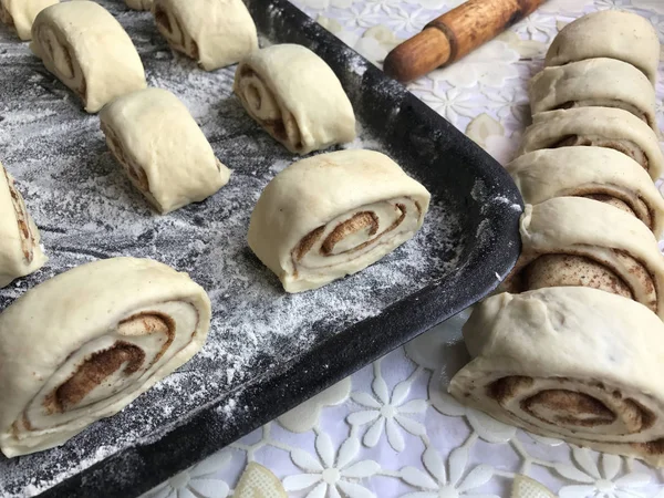Evde tarçın ile buns hazırlanması. Ham buns fırın tepsisine yalan. Tablo yanında bazı ham demir çubuklar ve ahşap bir oklava vardır.