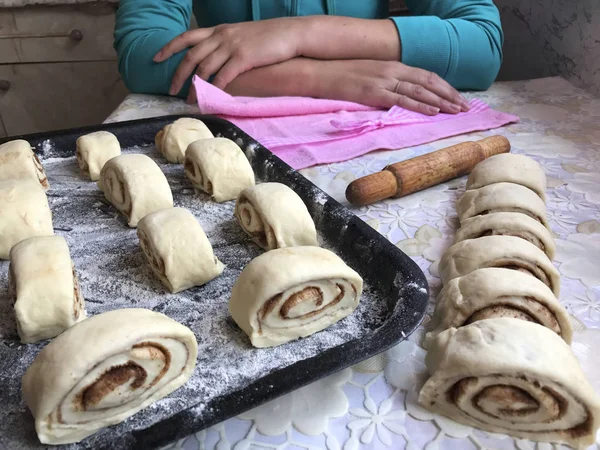 Evde tarçın ile buns hazırlanması. Ham buns fırın tepsisine yalan. Tablo yanında bazı ham demir çubuklar ve ahşap bir oklava vardır. Aşçı masada, ellerini sıktı oturur..