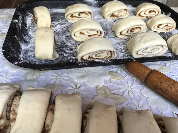Evde tarçın ile buns hazırlanması. Ham buns fırın tepsisine yalan. Tablo yanında bazı ham demir çubuklar ve ahşap bir oklava vardır.
