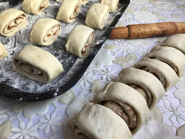 Zubereitung von Semmeln mit Zimt zu Hause. Rohe Brötchen liegen auf einem Backblech. Neben dem Tisch liegen ein paar rohe Knüppel und ein Nudelholz. — Stockfoto