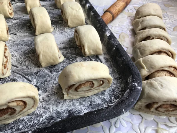 Zubereitung von Semmeln mit Zimt zu Hause. Rohe Brötchen liegen auf einem Backblech. Neben dem Tisch liegen ein paar rohe Knüppel und ein Nudelholz. — Stockfoto