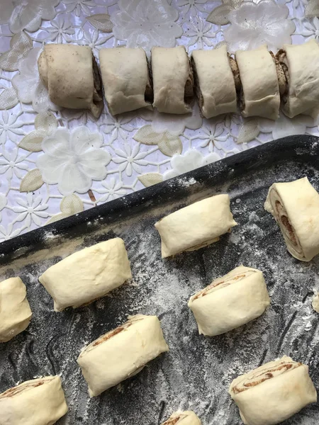 Evde tarçın ile buns hazırlanması. Ham buns fırın tepsisine yalan. Tablo yanında bazı ham demir çubuklar ve ahşap bir oklava vardır.