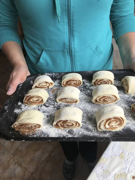 Evde tarçın ile buns hazırlanması. Kadın bir fırın tepsisi topuz ile rulo tutuyor.
