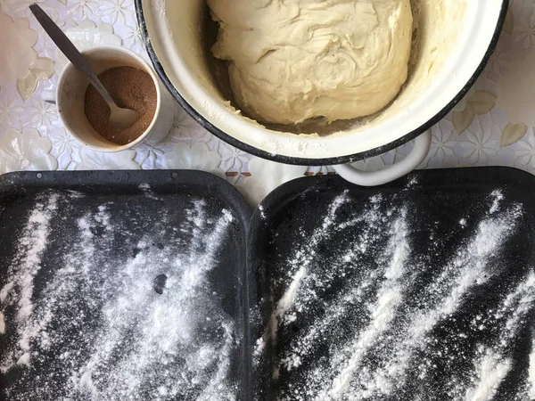 Evde tarçın ile buns hazırlanması. Tepsiyi un serpilir, hamur ve ahşap bir haddeleme pin masanın üstüne yalan. Tarçın şeker bir kupa ile.
