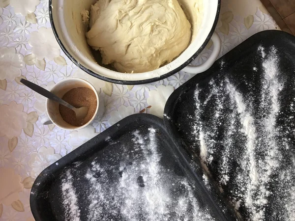 Persiapan roti dengan kayu manis di rumah. Baki ditaburi tepung, adonan dan kayu bergulir di atas meja. Kayu manis dengan gula di cangkir . — Stok Foto