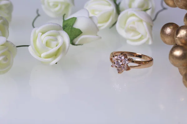 Διακοσμητικά για τους εορτασμούς. Χρυσό δαχτυλίδι με πέτρες και μπουκέτο των τεχνητών λουλουδιών. Σε λευκό φόντο. — Φωτογραφία Αρχείου