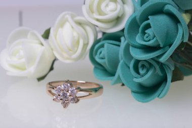 Kutlamalar için süsler. Altın yüzük taşlar ve yapay çiçekler buket. Gül beyaz bir arka plan üzerinde zümrüt.