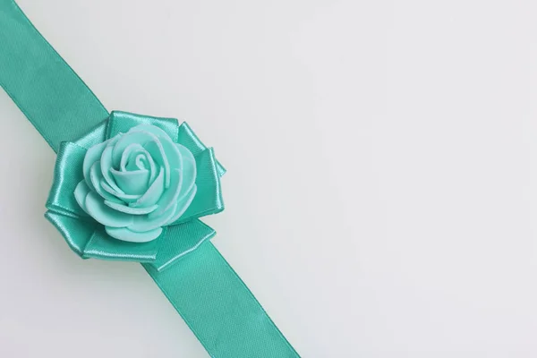 Decoração à mão na forma de uma rosa de cor esmeralda, costurada a uma fita de cetim. Em um fundo branco . — Fotografia de Stock