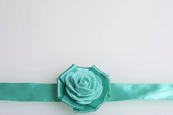 Decoração à mão na forma de uma rosa de cor esmeralda, costurada a uma fita de cetim. Em um fundo branco . — Fotografia de Stock