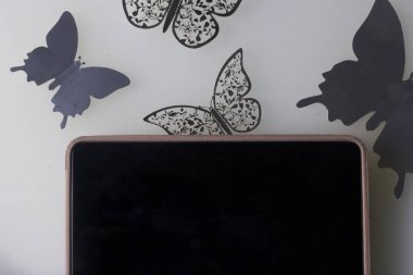 Tablet beyaz bir yüzeye yatıyor. Onun etrafında süsler kelebek, kesim folyo.