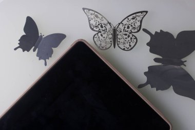 Tablet beyaz bir yüzeye yatıyor. Onun etrafında süsler kelebek, kesim folyo.