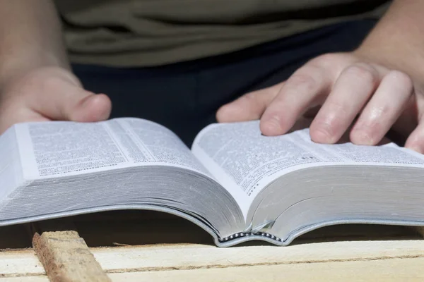 Un joven lee la Biblia, colocándola sobre una tabla de madera . — Foto de Stock