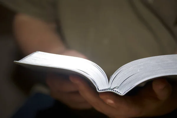 Un joven lee la Biblia. Tiene un libro abierto en sus manos. . — Foto de Stock