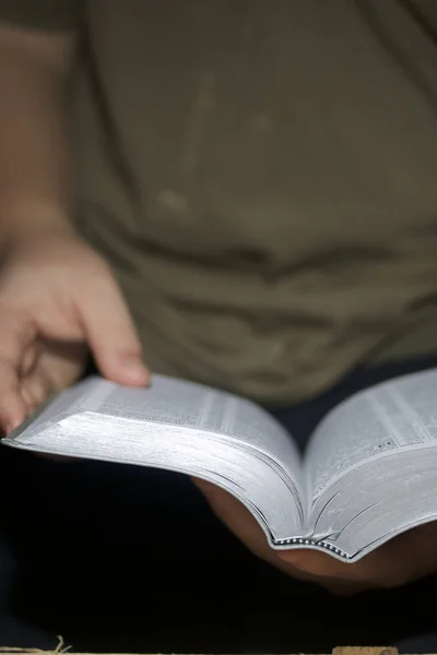 Un joven lee la Biblia. Tiene un libro abierto en sus manos. . — Foto de Stock