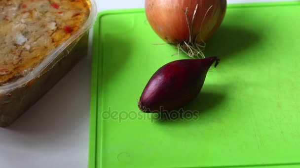 Un hombre limpia una cebolla roja con un cuchillo. Junto a ella hay una tabla de cortar y un forshmak hecho de pescado . — Vídeos de Stock