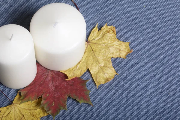 Свічки стоять на опале осіннє листя різних кольорів. Все це на тканинному сірому фоні . — стокове фото