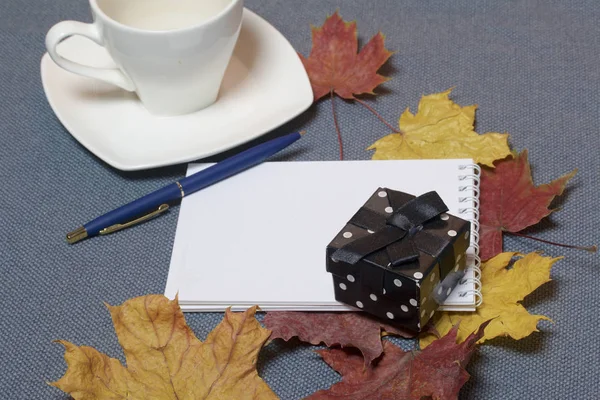 Bougeoir en métal forgé avec bougies. Il y a un bloc-notes ouvert et un stylo. Une tasse avec du café non approuvé. Les feuilles tombées en automne de jaune et de rouge sont éparpillées à la surface . — Photo